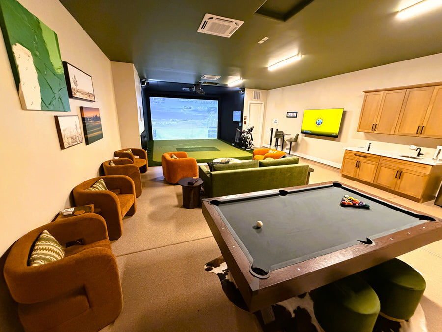 Golf simulator room with pool table, chairs, and a large screen TV.