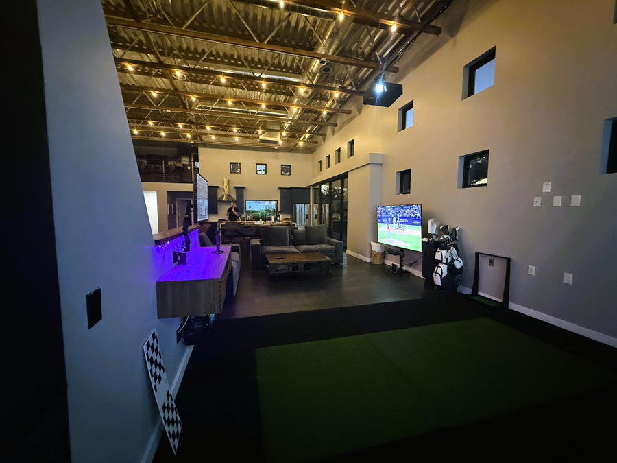 Indoor recreational area with multiple screens displaying different content, including a golf simulator.