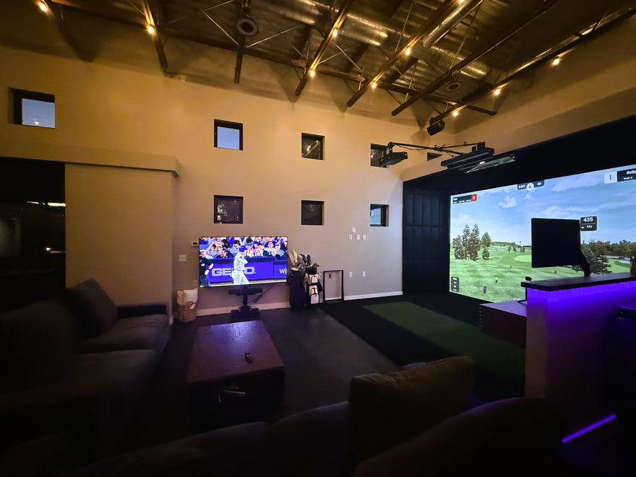 Golf simulator with two screens, surrounded by furniture.