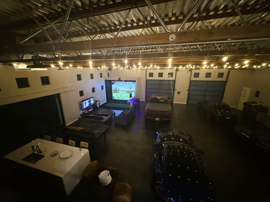 Indoor golf simulator with cars, a TV, and string lights on the ceiling.