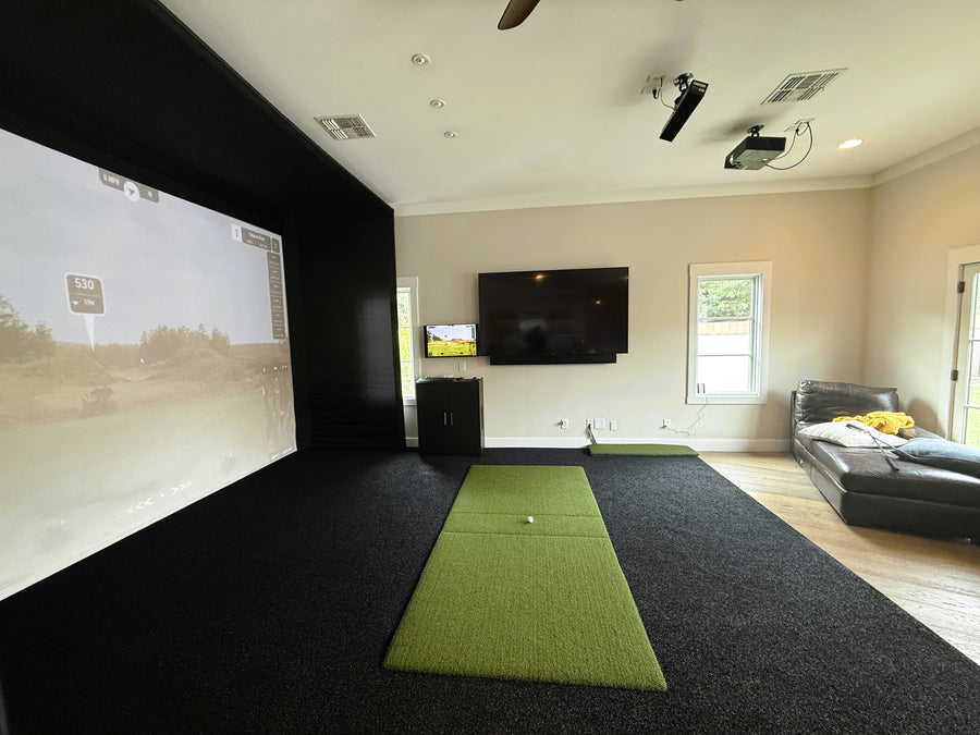 Indoor golf simulator setup in a room with a screen, mat, and TV.