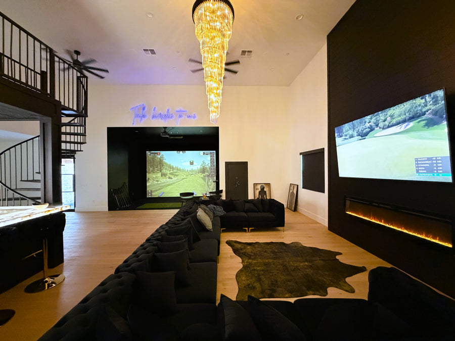 Modern living room with two TVs, a staircase, and an indoor golf simulator.
