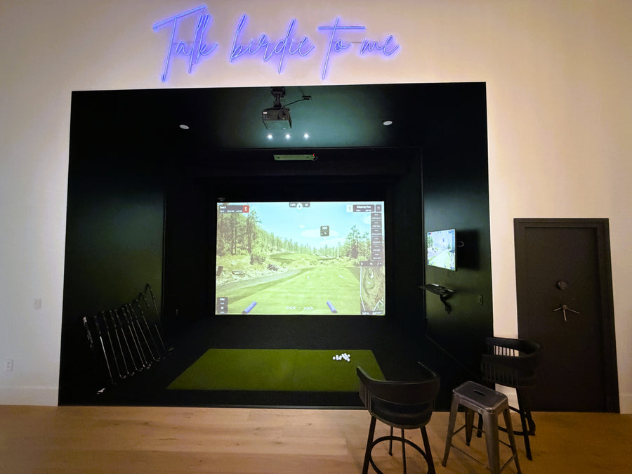 Golf simulator setup in a room with a large screen displaying a golf course.