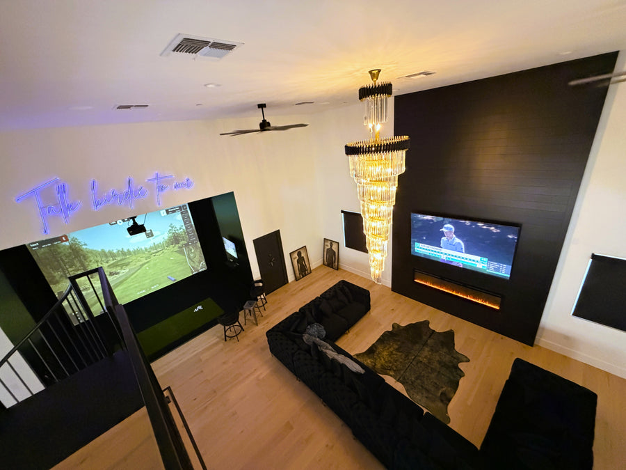Modern living room with large TV, golf simulator, chandelier, and decorative elements.