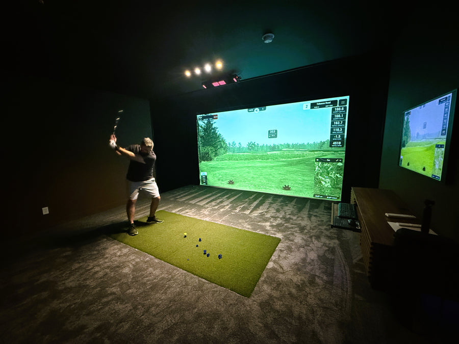 Person playing on golf simulator in a dark room with two screens.