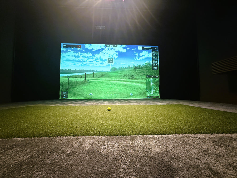 Golf simulator setup with screen displaying a golf course on a grass-covered floor.