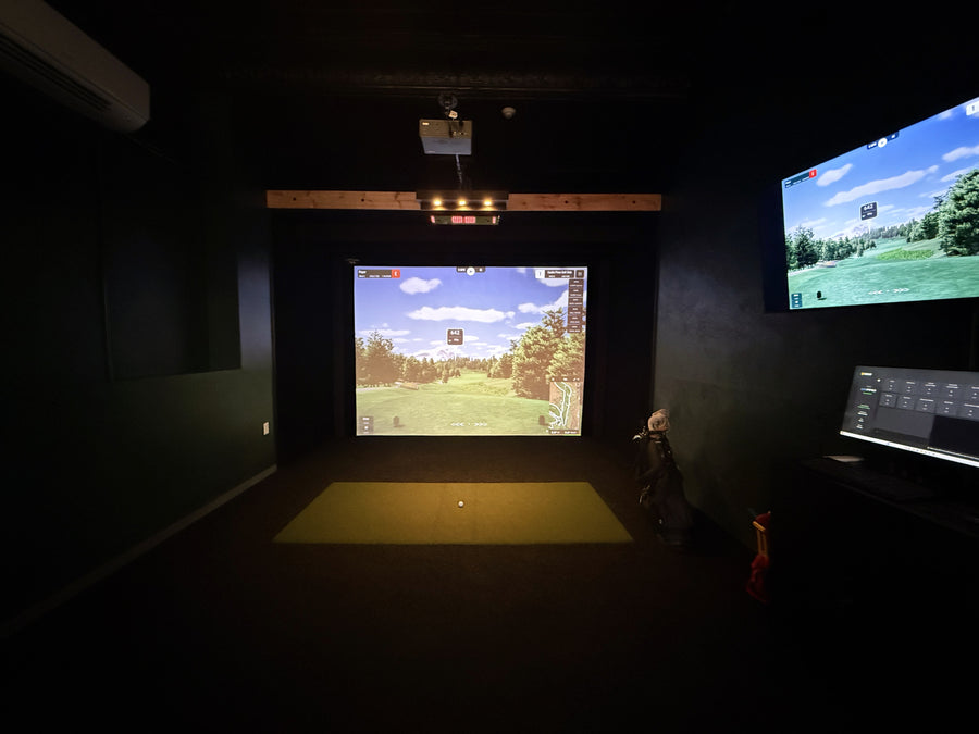 Indoor golf simulator setup with two screens displaying a golf course.