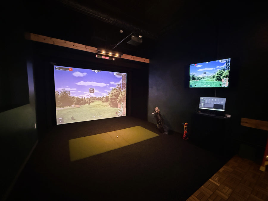 Golf simulator setup with large screen and laptop in a dark room