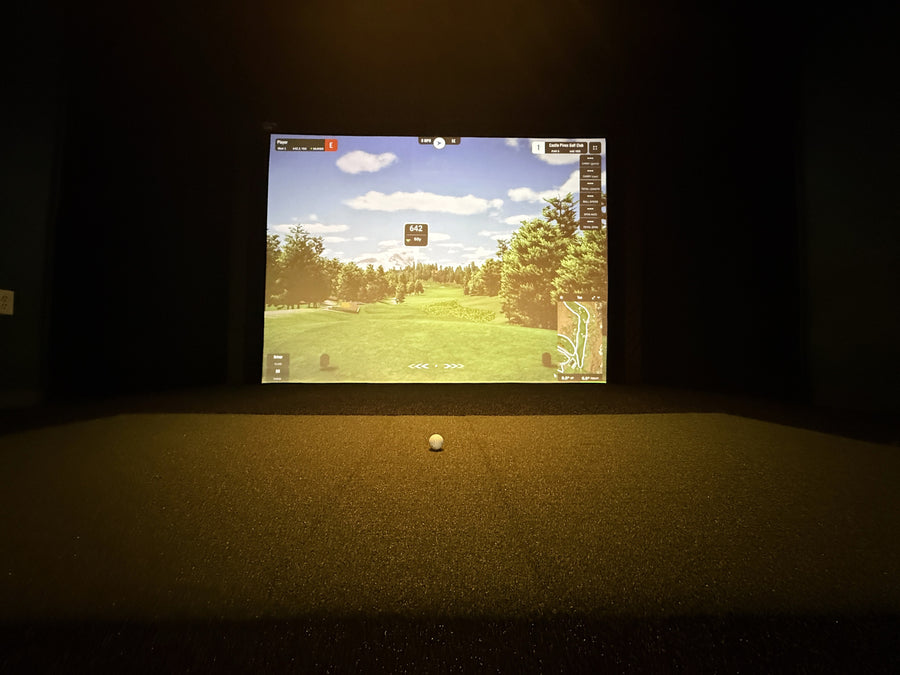 Golf simulator setup with screen displaying a golf course and a ball on a dark floor.