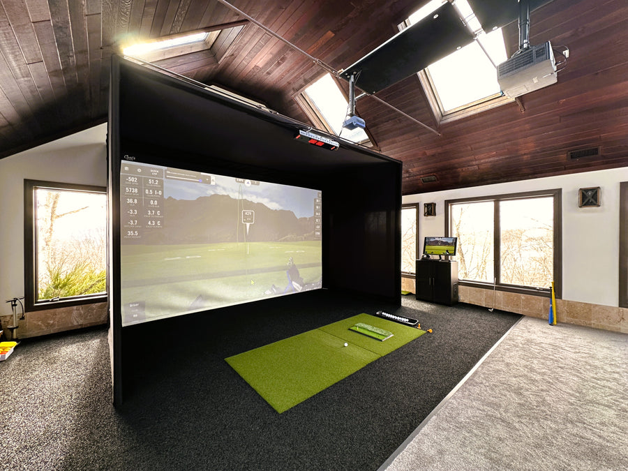 Indoor golf simulator setup with screen, projector, and mat in a room with wooden ceiling.