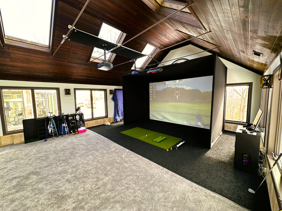 Indoor golf simulator setup in a room with a large screen and various equipment.