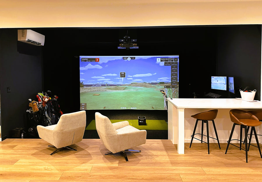 Golf simulator setup in a room with chairs and a counter.
