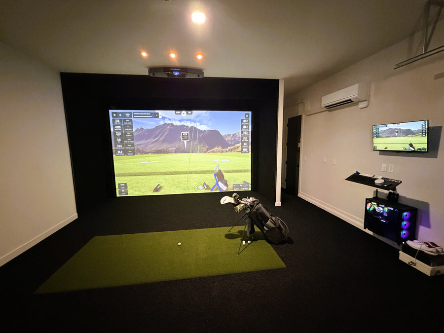 Golf simulator setup with screen, golf club, and ball on a green mat.