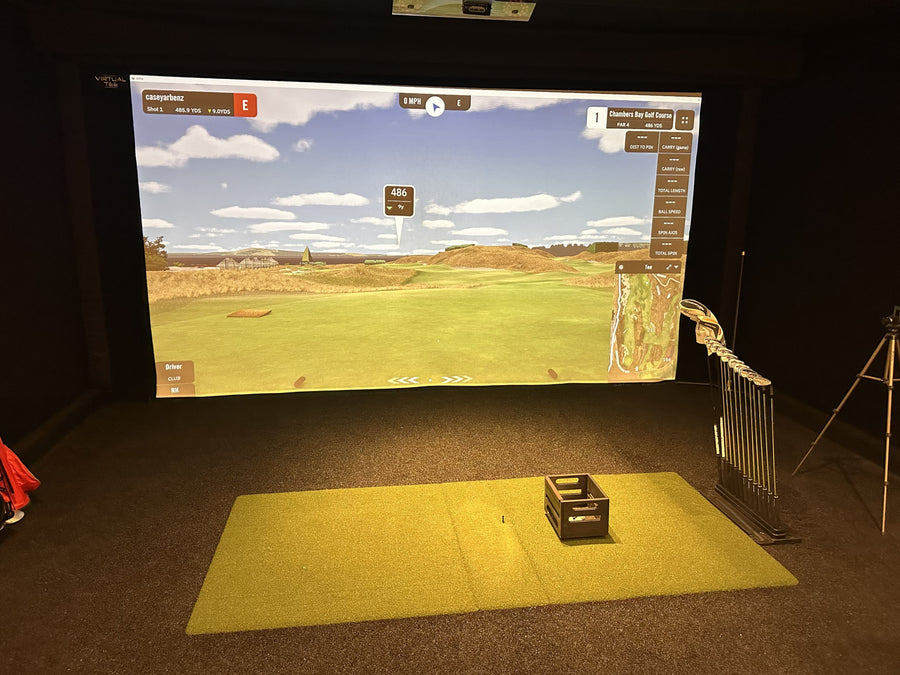 Golf simulator setup with screen displaying a golf course and mat on the floor.