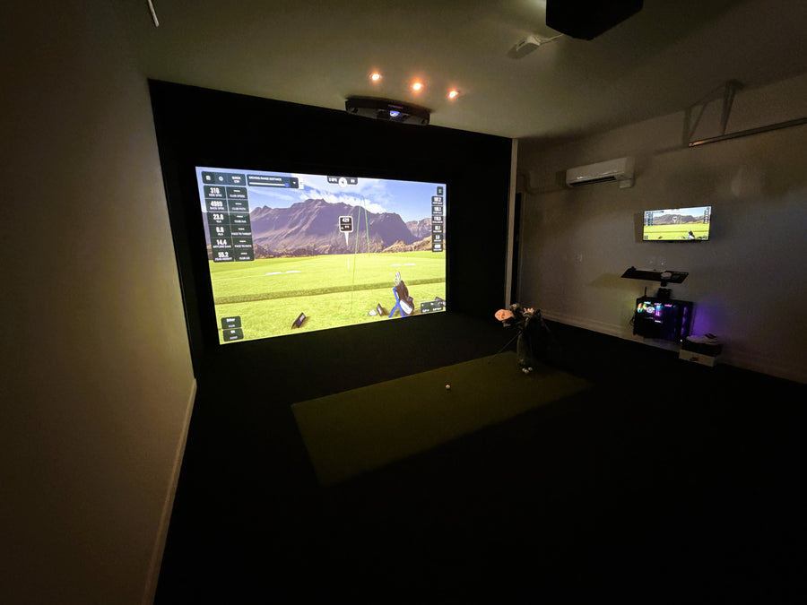 Indoor golf simulator setup with large screen displaying a golf course.