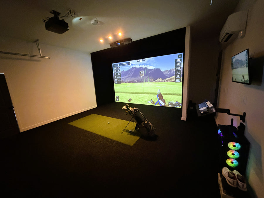Golf simulator setup with screen displaying a golf course, golf club, and mat on the floor.