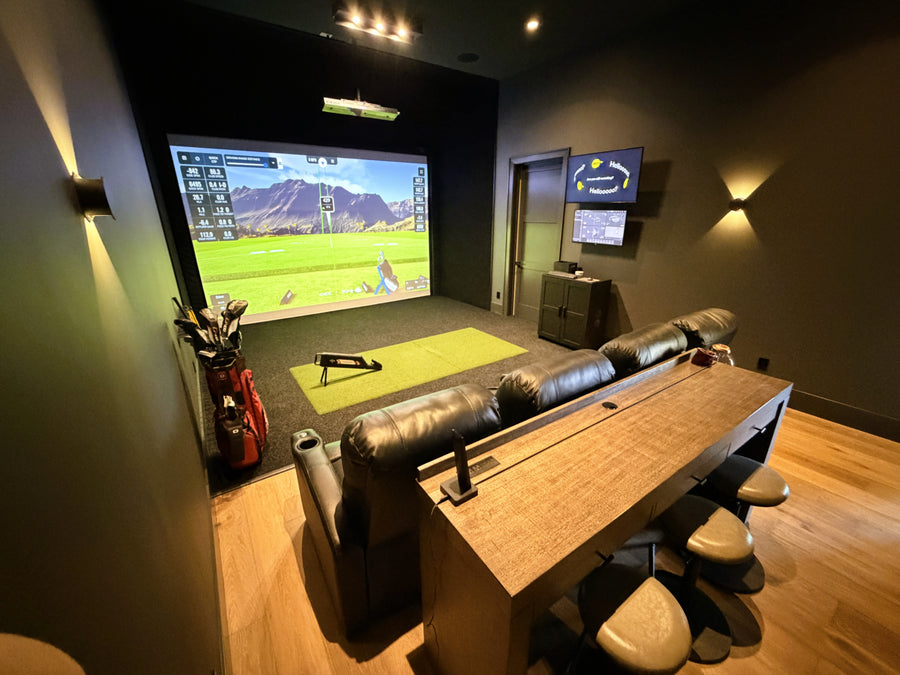 Home golf simulator room with a large screen displaying a sports game, surrounded by furniture and decor.