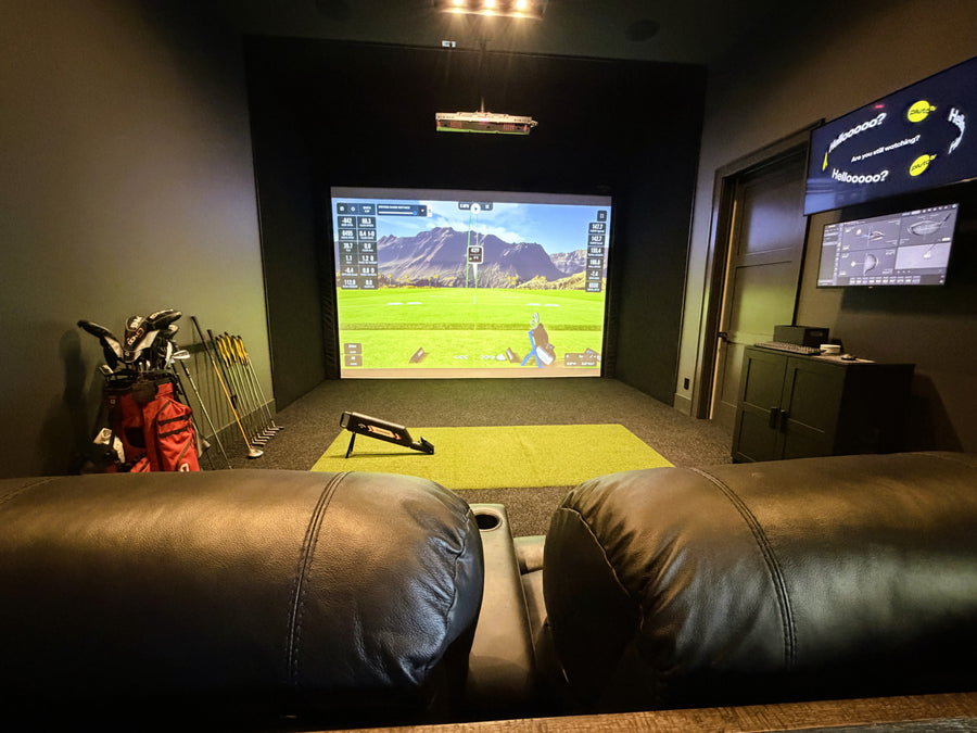 Indoor golf simulator setup with two screens, a couch, and golf equipment.