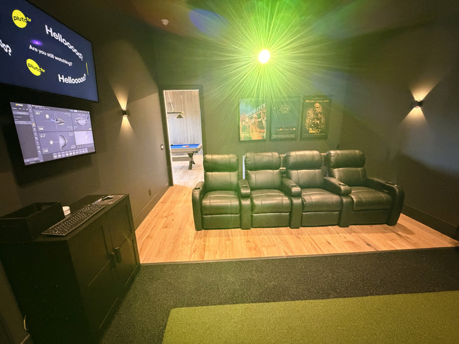 Green leather sofa in a golf simulator and theater room with two screens displaying software interfaces.
