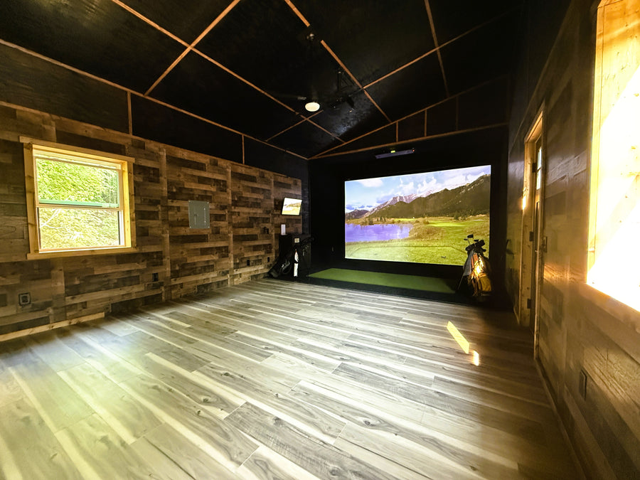 Indoor golf simulator shed with wooden walls and floor, featuring a screen displaying a golf course.