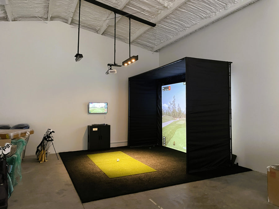 Indoor golf simulator setup with screen and equipment in a room.