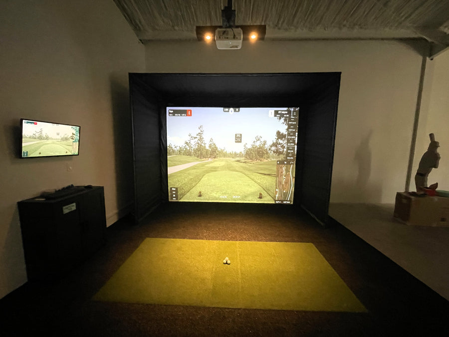 Indoor golf simulator setup with two screens displaying a golf course.