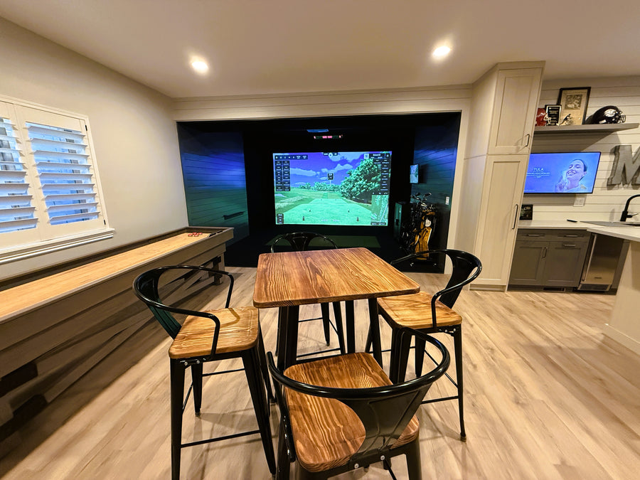 Game room with a golf simulator, surrounded by chairs and a table.