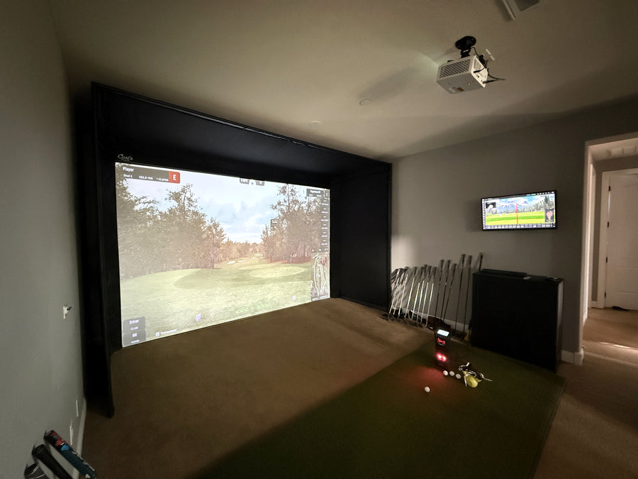 Golf simulator setup in a room with a large screen and projector.