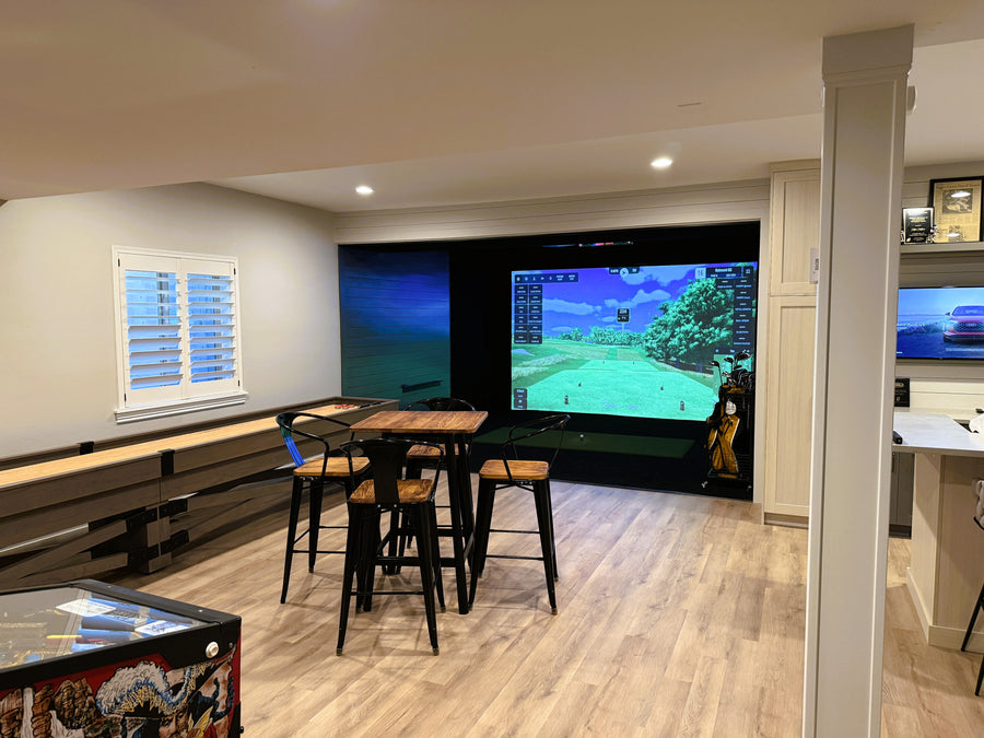Game room with a golf simulator, surrounded by wooden flooring and furniture.