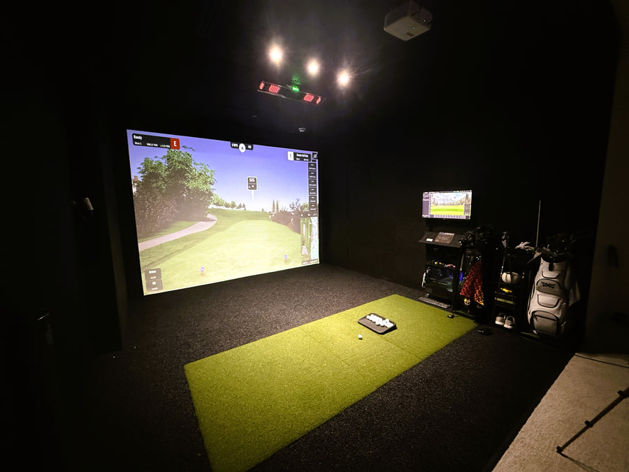 Indoor golf simulator setup with screen displaying a golf course and various equipment.