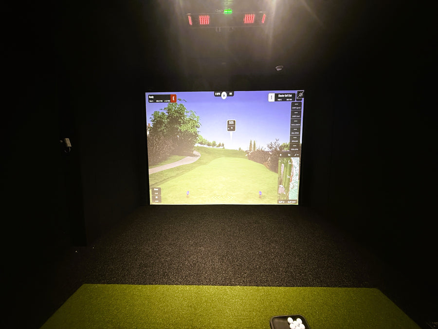Golf simulator setup with screen displaying a golf course on a dark floor.