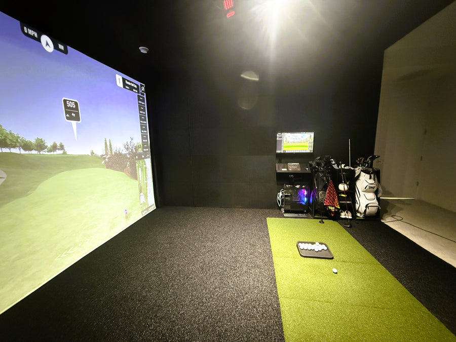 Golf simulator room with screen displaying a golf course and golf clubs on a stand.