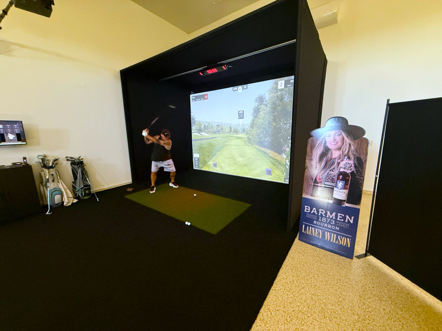 Golf simulator setup in a room with a screen displaying a golf course.
