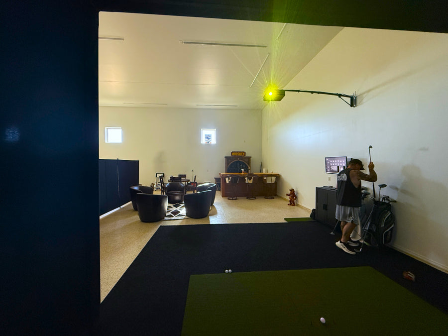 Indoor golf simulator setup with a person using it, surrounded by various equipment.