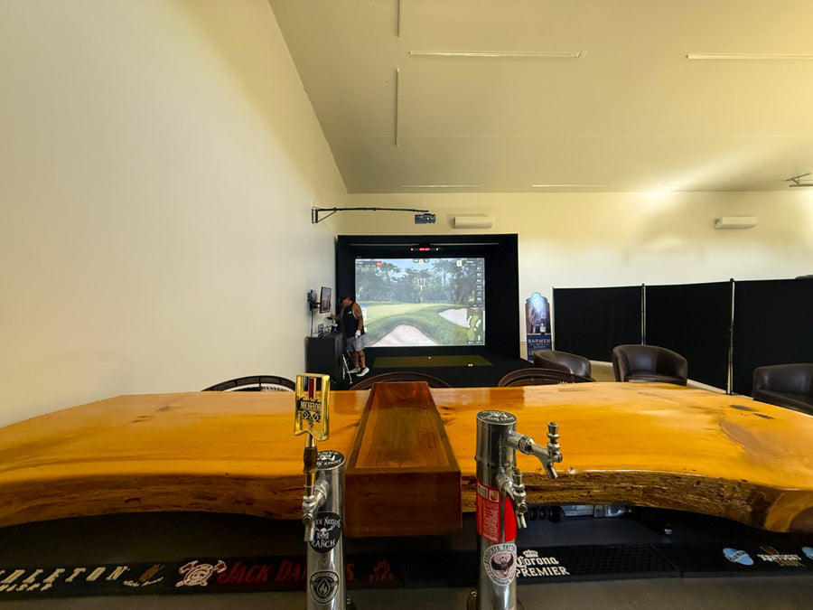 Long wooden table with metal legs in a golf simulator space.