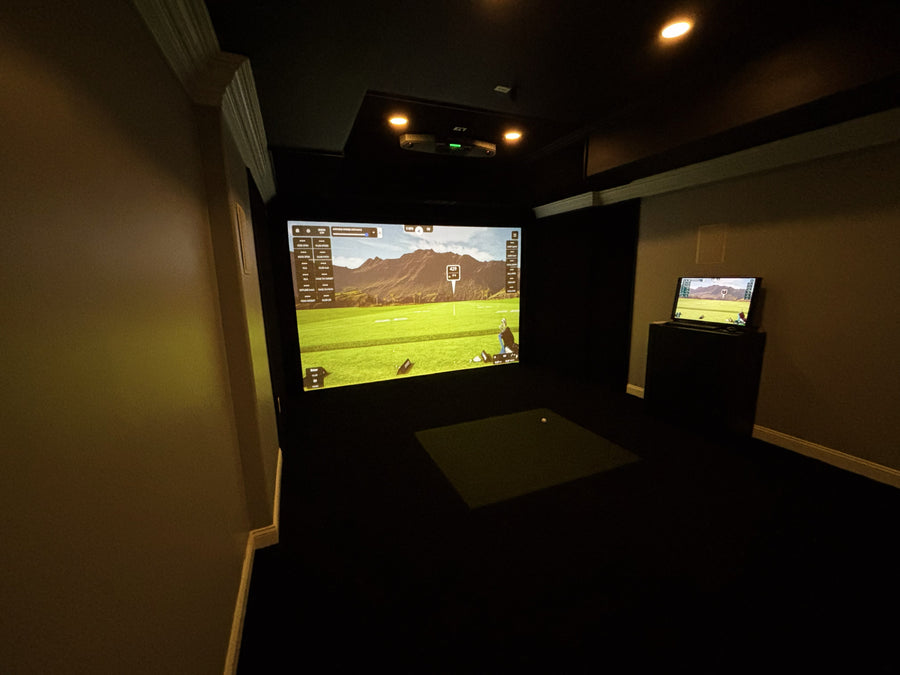 Golf simulator setup in a dark room with two screens displaying a golf course.