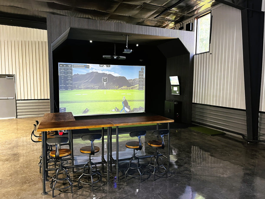 Indoor golf simulation setup with a large screen displaying a virtual golf game.