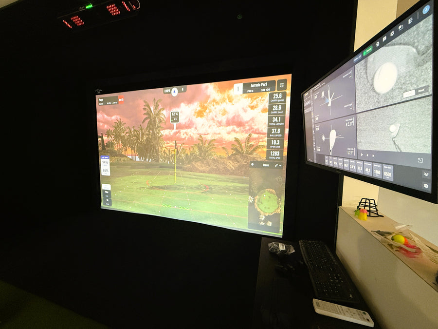 Two computer monitors displaying a golf simulation game in a golf simulator space.