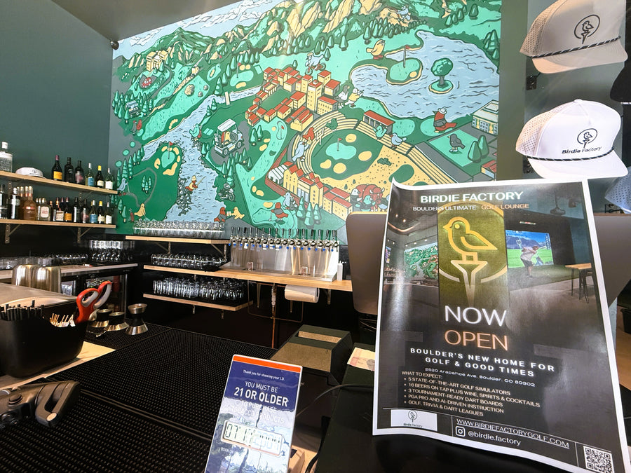 Bar area with a large map on the wall, bottles on shelves, and promotional signs for 'Birdie Factory'.