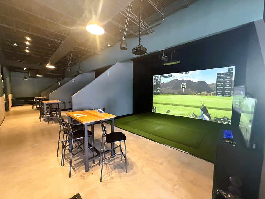 Indoor recreational area with a large screen displaying a golf simulation game.