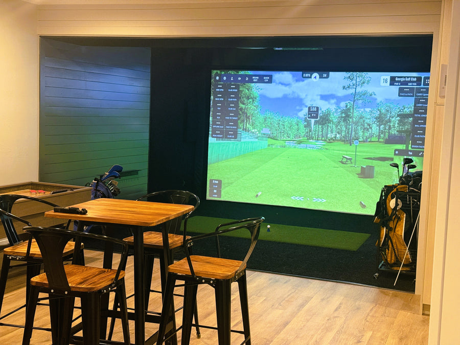 Golf simulator setup in a room with a large screen displaying a golf course.