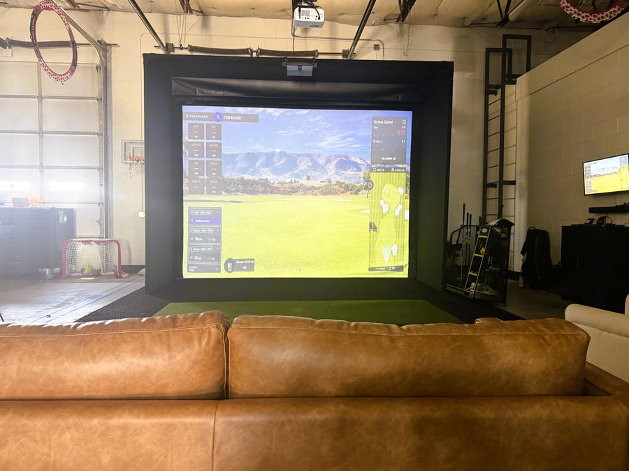 Golf simulator setup in a warehouse with a large screen and couch.