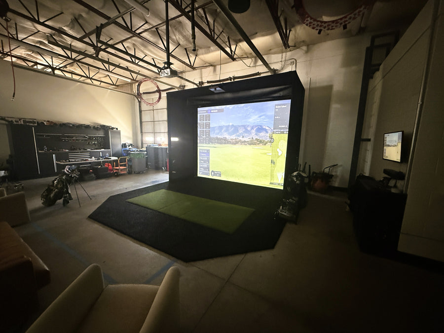 Indoor golf simulator setup with large screen displaying a virtual sports field.