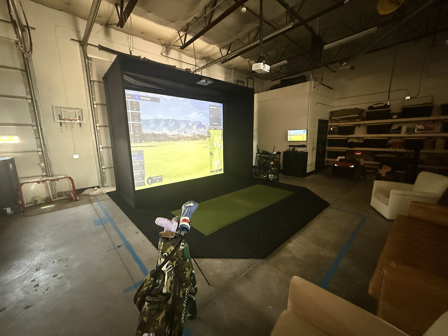 Indoor golf simulator setup in a room with a screen displaying a golf course.