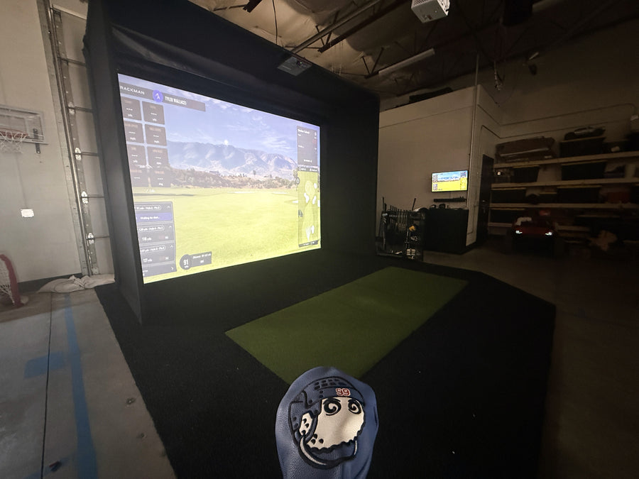 Golf simulator setup with screen displaying a golf course in an indoor facility.
