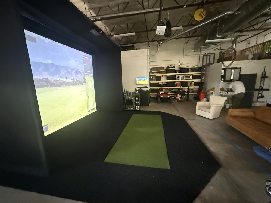Indoor golf simulator setup in a room with a screen displaying a golf course.