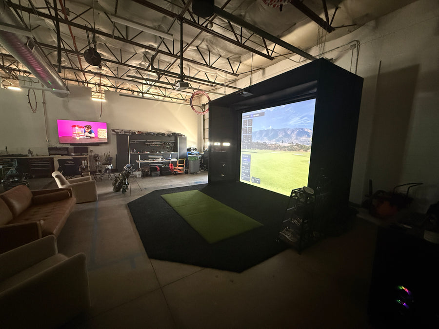 Indoor golf simulator setup with large screen displaying a sports field.