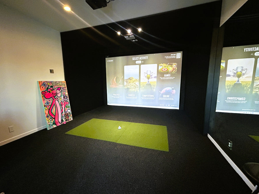 Indoor golf simulator setup with two screens displaying golf-related graphics on a dark floor.