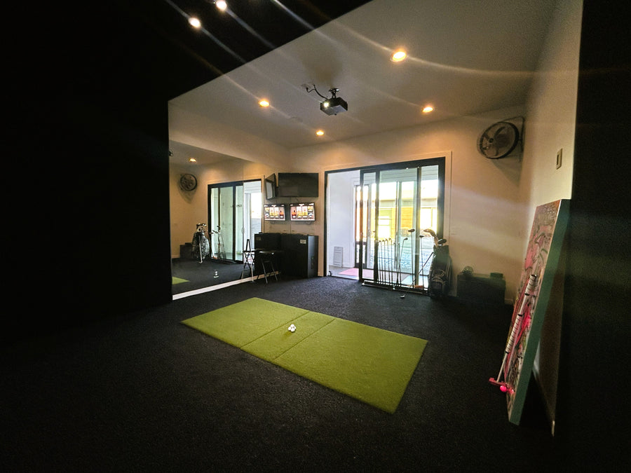 Indoor golf simulator room with a green mat on the floor and a TV in the background.
