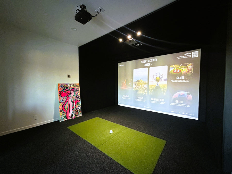Indoor golf simulator setup with screen displaying game options and green mat on floor.